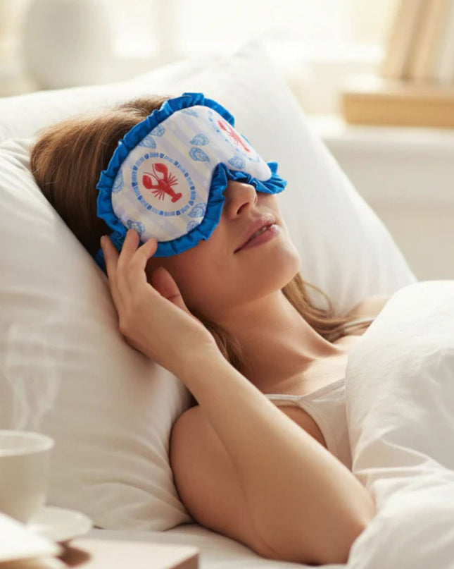 Woman lying in bed wearing a lobster-themed sleep mask.