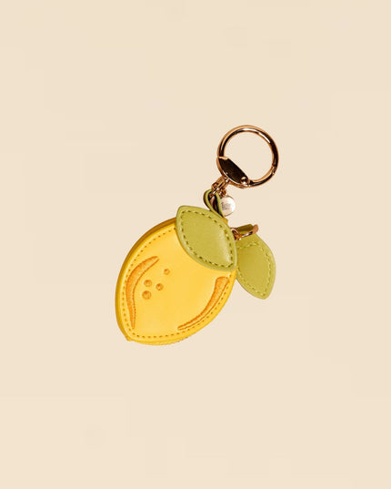 Yellow lemon-shaped keychain with green leaves on a beige background