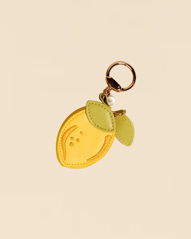 Yellow lemon-shaped keychain with green leaves on a beige background