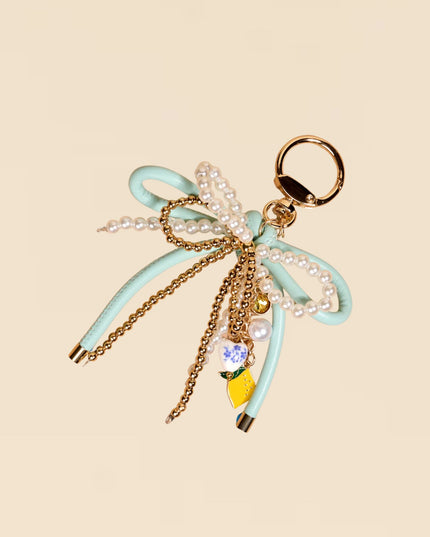 Decorative keychain with bow, lemon charm, and pearl details on a beige background