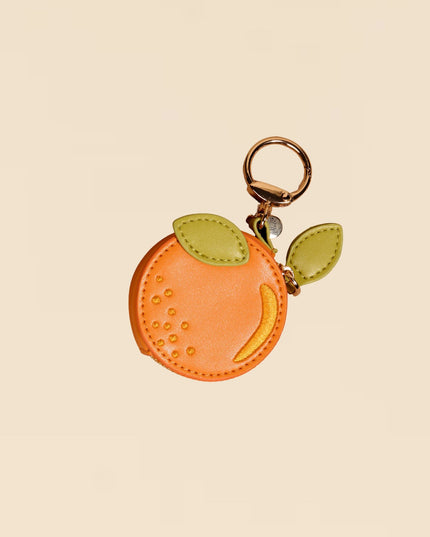 Peach-shaped keychain with a gold ring on a beige background
