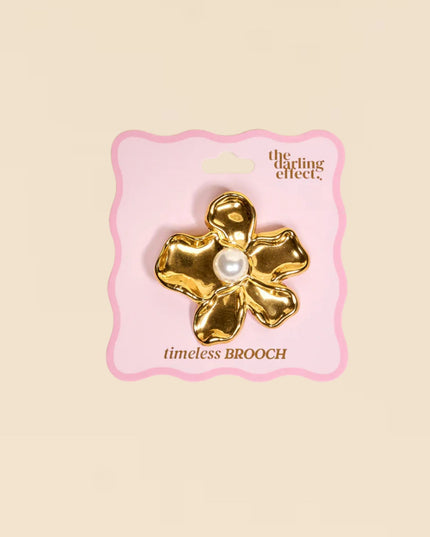 Gold brooch with pearl center on a pink card labeled 'the crafting effect' against a beige background