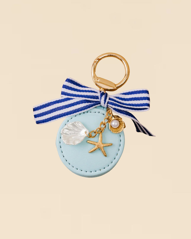 Keychain with blue ribbon, seashell, and starfish charm on a beige background