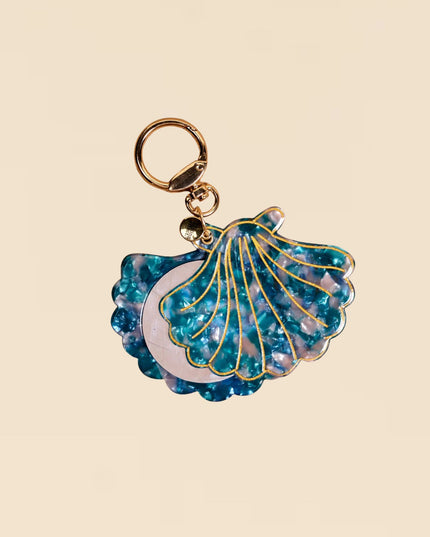 Blue shell-shaped keychain with gold accents on a beige background