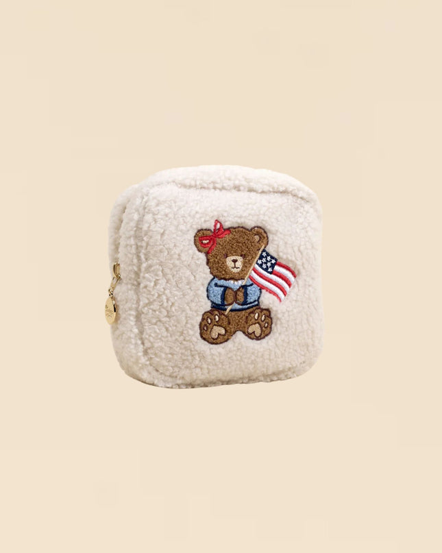 Small cream-colored pouch with a teddy bear design featuring an American flag on a beige background