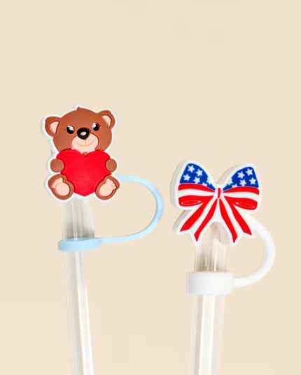 Two decorative items on a beige background: a teddy bear with a red heart and a bow with the American flag design.