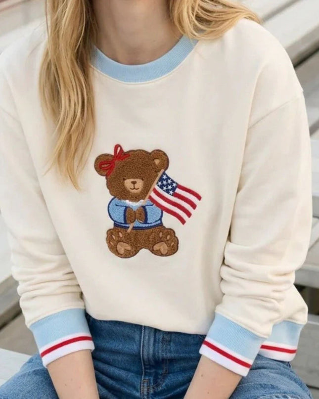 Person wearing a sweater with a teddy bear design holding an American flag.