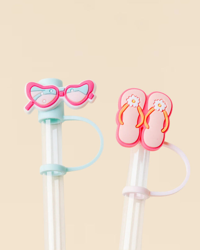 Two novelty straws with a pair of pink sunglasses and a pair of pink flip-flops on a beige background.