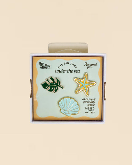 Set of three pins featuring a monstera leaf, starfish, and shell design in a decorative box.