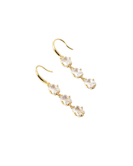 A pair of gold drop earrings with three clear, bezel-set round gemstones on each earring, displayed against a solid white background.