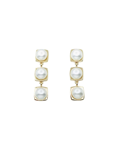 A pair of gold drop earrings featuring three stacked square bezel-set white pearls on a solid white background.