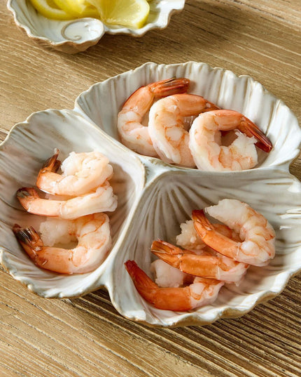 Three-shell dish with cooked shrimp on a wooden surface