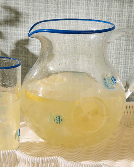 Clear glass pitcher and glasses filled with a yellow beverage on a textured surface.