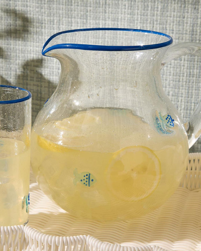 Clear glass pitcher and glasses filled with a yellow beverage on a textured surface.