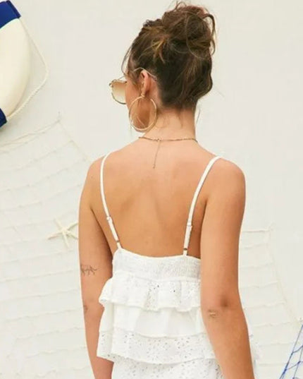A woman shown from behind wearing a white ruffled eyelet spaghetti-strap top, standing against a white wall with nautical decor like a life preserver and netting.